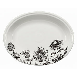 The Fiesta Botanical Floral Black 11 5/8 Inch Medium Oval Serving Platter features a white ceramic base with a black botanical floral design of detailed flowers and leaves along one edge.