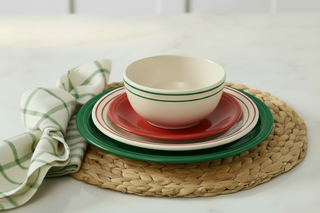 A stacked Americana Scarlet Band Classic Bistro 3-Piece Dinnerware Set featuring a bowl, small plate, and dinner plate on a woven placemat with a green and white plaid napkin.
