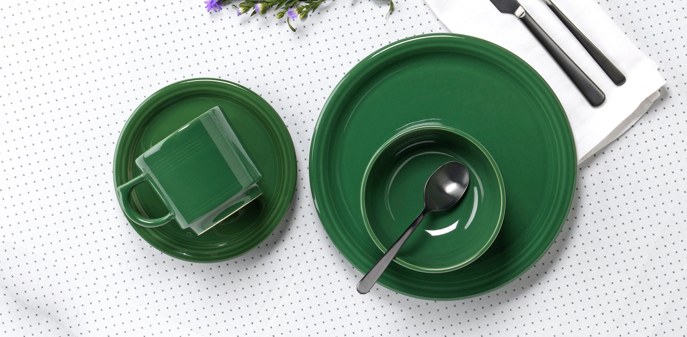 4 piece place setting in Jade color. Place setting is set on white and black patterend tablecloth. Also on the table is flatware and purple flower