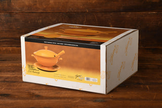 A white box with orange graphics displays the Marigold 75th Anniversary Soup Tureen on the front. The box, part of the Marigold Limited Edition from the Fiesta Factory Direct museum collection, sits on a wooden surface and features the brand Fiesta Factory Direct, with an image of the soup tureen taking up most of the visible side.