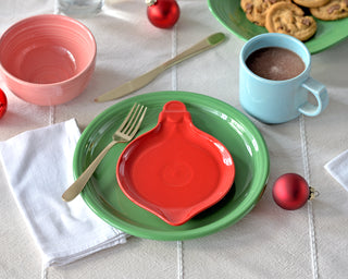 Colorful table setting with a green plate, red ornament shaped plate, and blue mug on a white tablecloth.