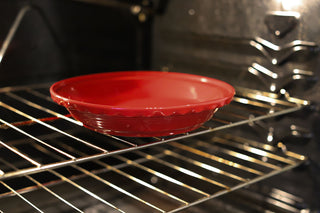 A Fiesta 10 1/4 Inch Deep Dish Pie Baker (44OZ) by Fiesta, in red ceramic and made in the USA, sits empty on the oven’s middle rack. The oven-safe baker is ready for your next favorite recipe.