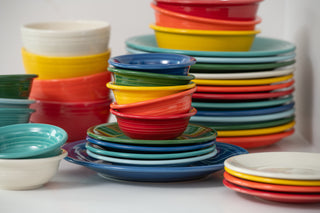 Stacks of multicolored ceramic dishes, including plates and bowls in red, yellow, green, blue, and turquoise, arranged in a casual display.