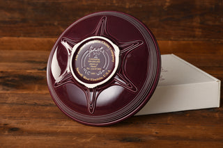 A Raspberry Presentation Bowl by Fiesta Factory Direct, circular in shape and engraved to mark the 500 millionth piece, reminiscent of a prized Fiesta collectible, rests on a white box atop a wooden surface.
