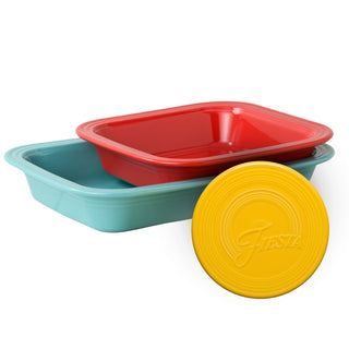 Two rectangular Fiesta Factory Direct Bakers in turquoise and red are stacked, with a round yellow “Fiesta” embossed trivet in front.