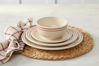 Cream dinnerware with red bands and red plaid napkin on rattan placemat over marble