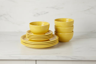 The Retired Bistro Coupe 12-Piece Dinnerware Set by Fiesta, featuring bright yellow plates and bowls, is stylishly stacked on a white marble countertop with a matching backsplash.